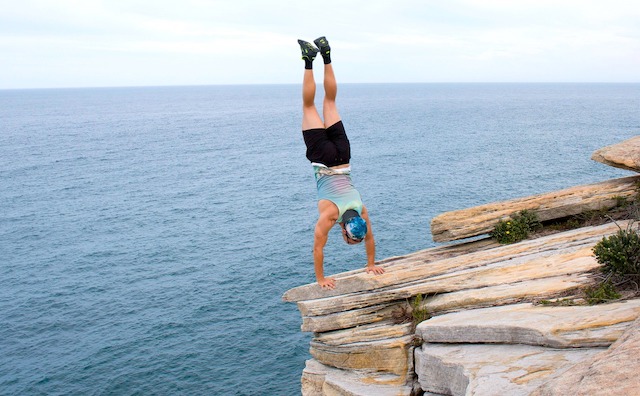 person doing handstand on seaside cliff edge